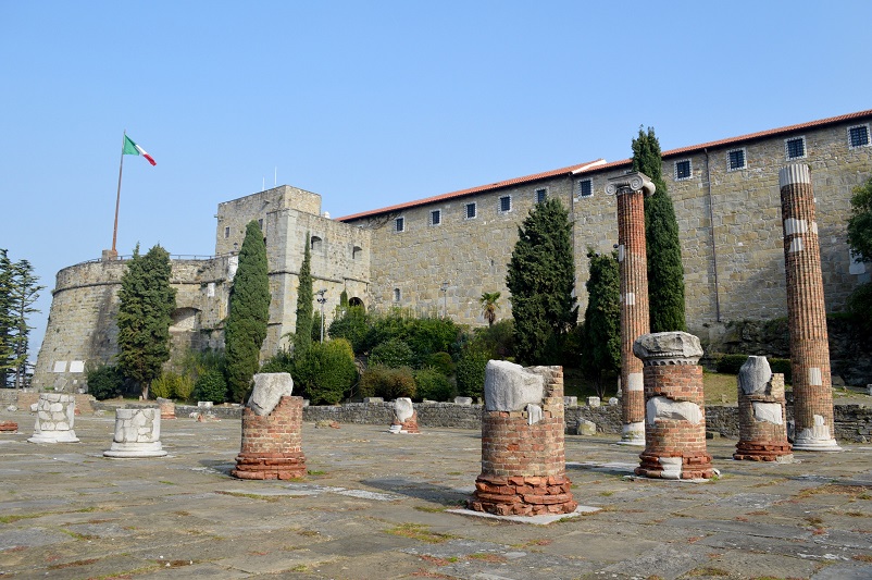 piloni vechi de cărămidă în fața unui castel care arborează steagul Italian, Trieste