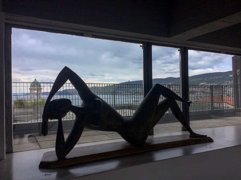 sculptura unei femei rabatabile în fața unei ferestre largi pe malul apei Trieste