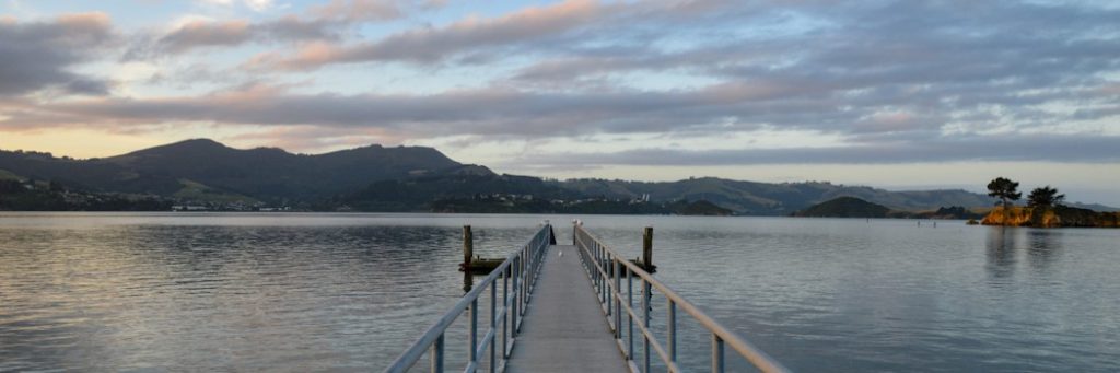 A dock leading out onto a still lake with a low mountain backdrop at sunset